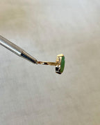side view of gold ring with green stone, help by silver tool above light beige fabric background 