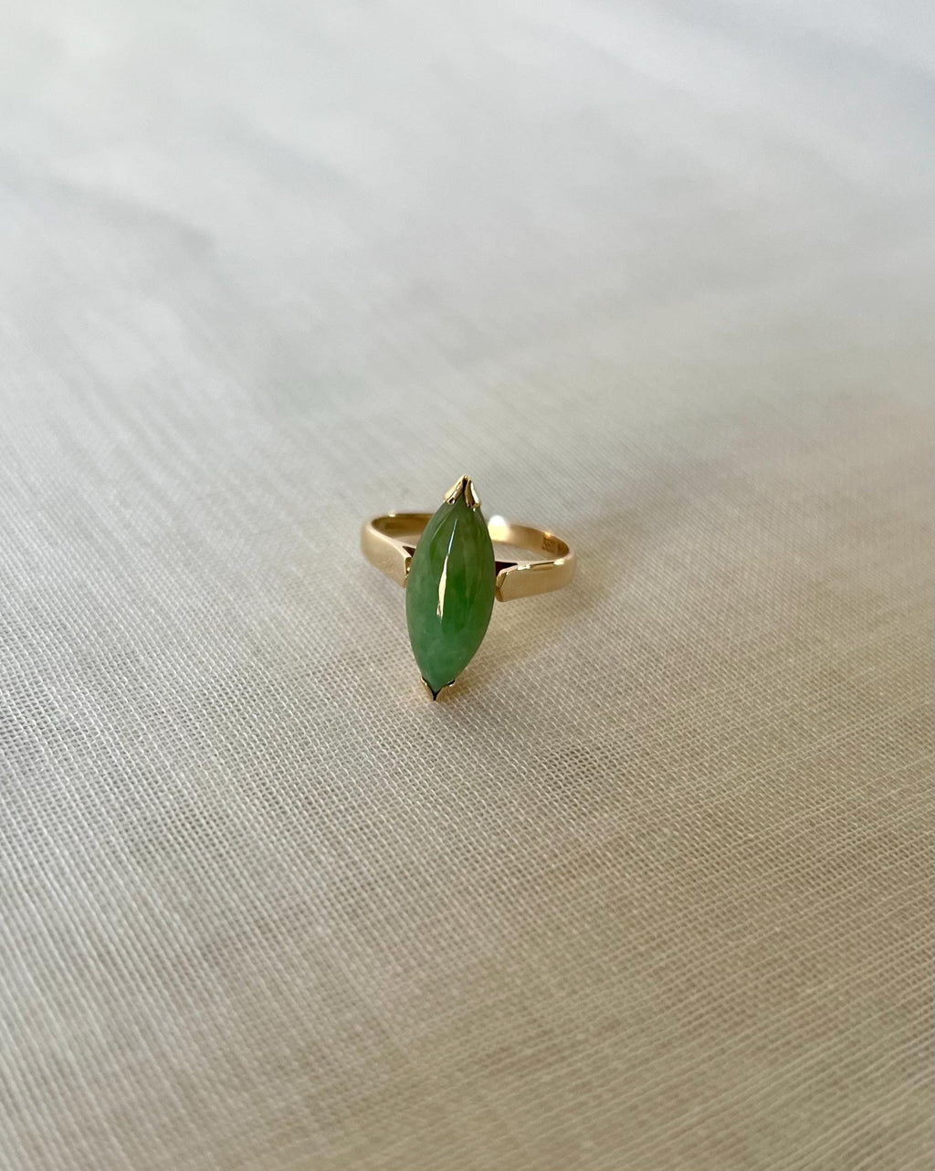 Gold ring with a marquise shape green jade gemstone on a light beige fabric background