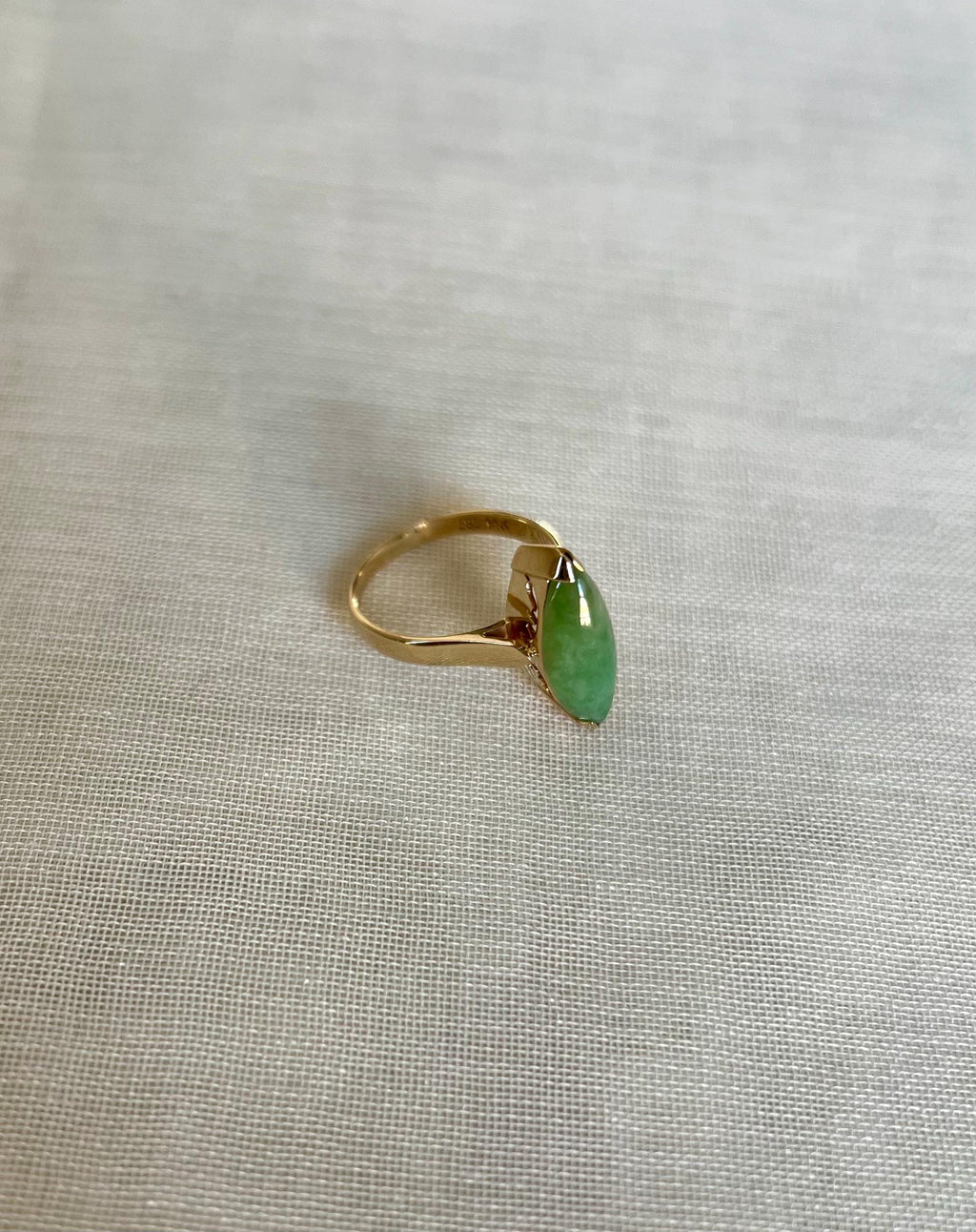 Gold ring with a green gemstone on a light beige fabric background