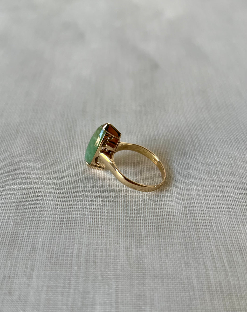 side view of green stone gold ring on light beige fabric background 