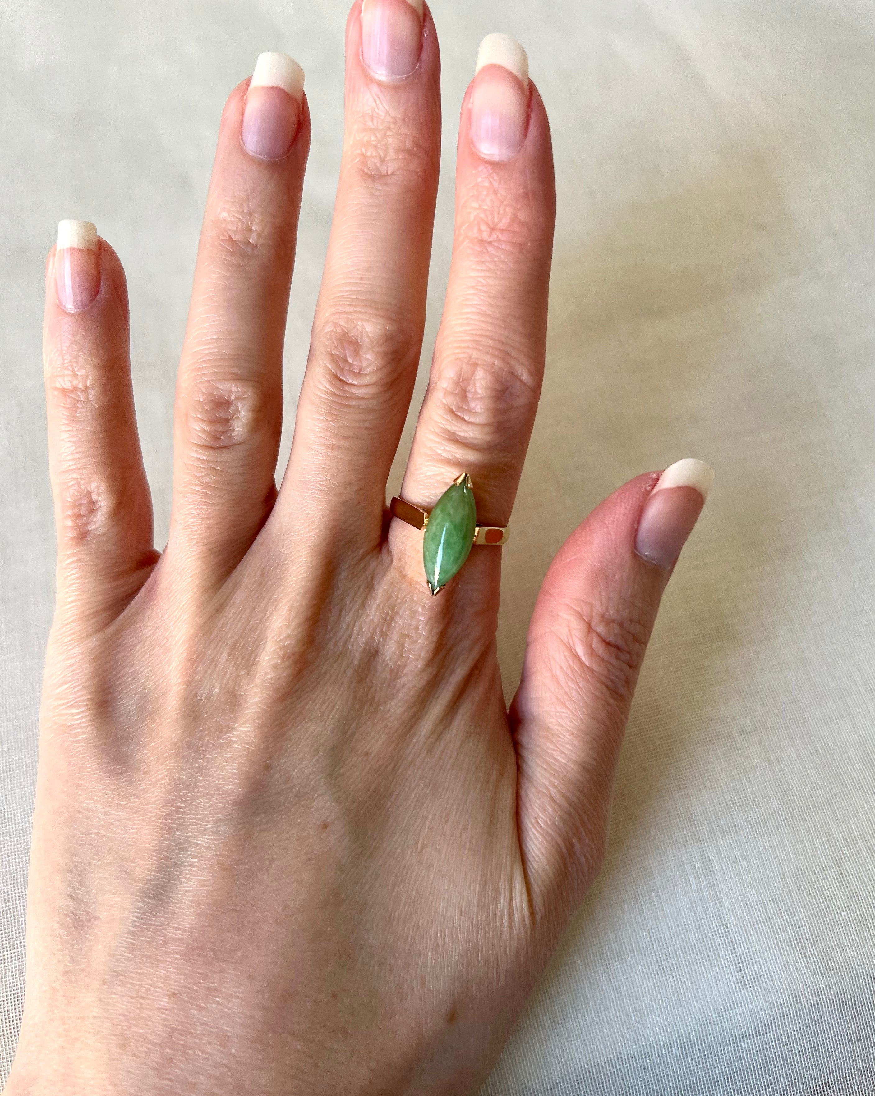 A gold ring with a marquise-cut green gemstone worn on a person's finger, shown against a light beige fabric background.