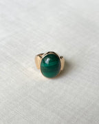 A gold ring with an oval green malachite stone, resting on a textured white fabric background.