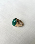 A gold ring featuring an oval-shaped green malachite stone, resting on a textured white fabric background.