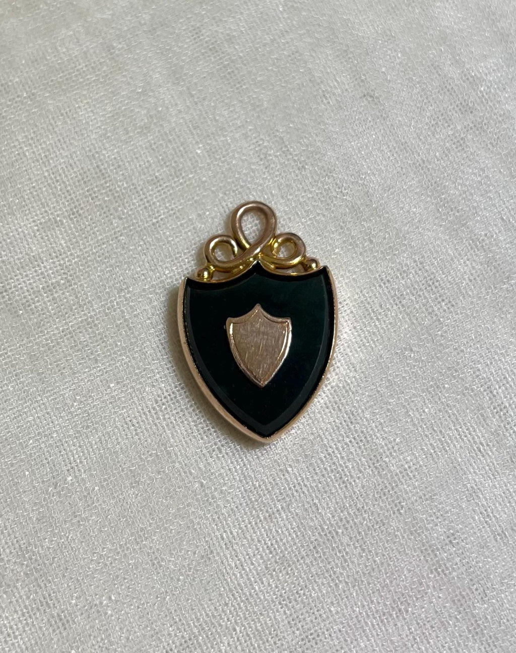 gold pendant in shape of shield set with dark green bloodstone, resting on white fabric background