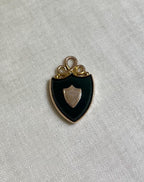 gold pendant in shape of shield set with dark green bloodstone, resting on white fabric background