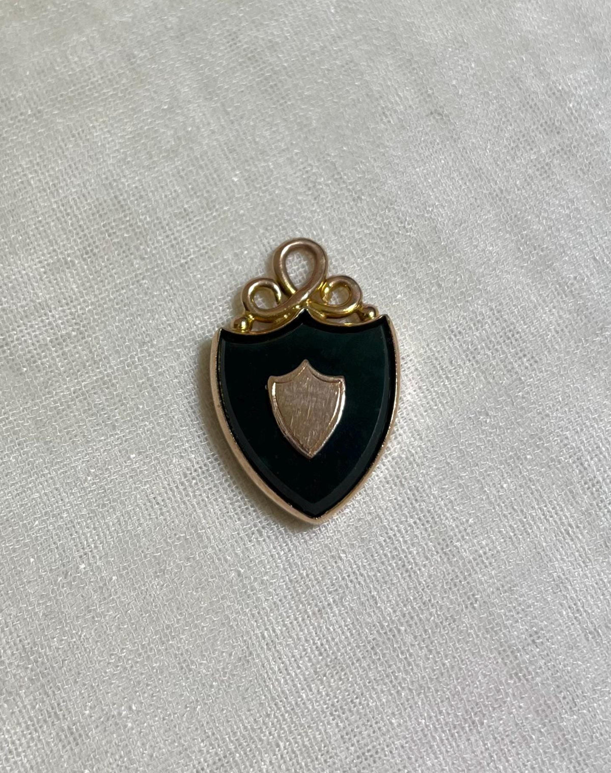 gold pendant in shape of shield set with dark green bloodstone, resting on white fabric background