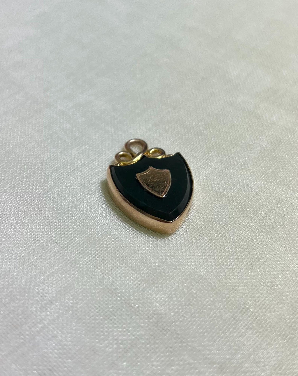 gold shield shaped pendant with deep green almost black bloodstone, on white fabric background