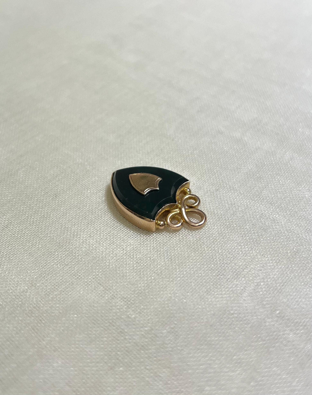 shield shaped gold and black pendant on white fabric background