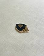 shield shaped gold and black pendant on white fabric background