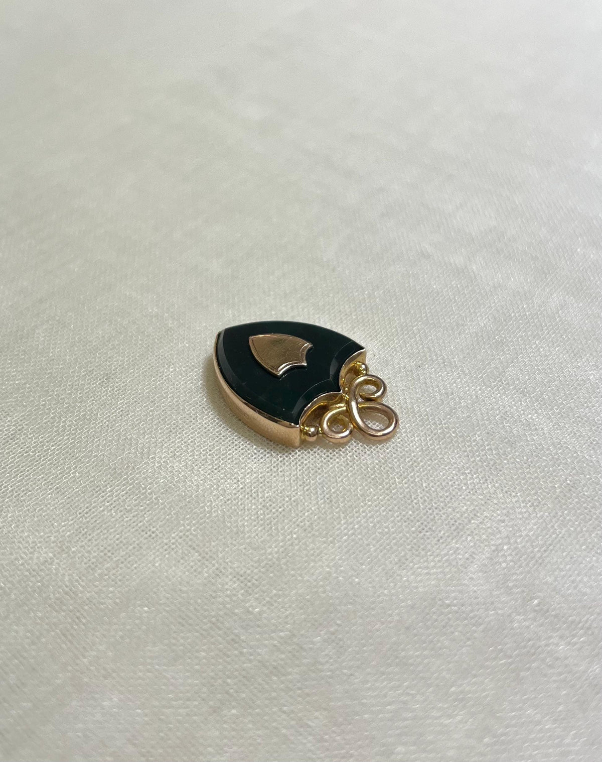 shield shaped gold and black pendant on white fabric background