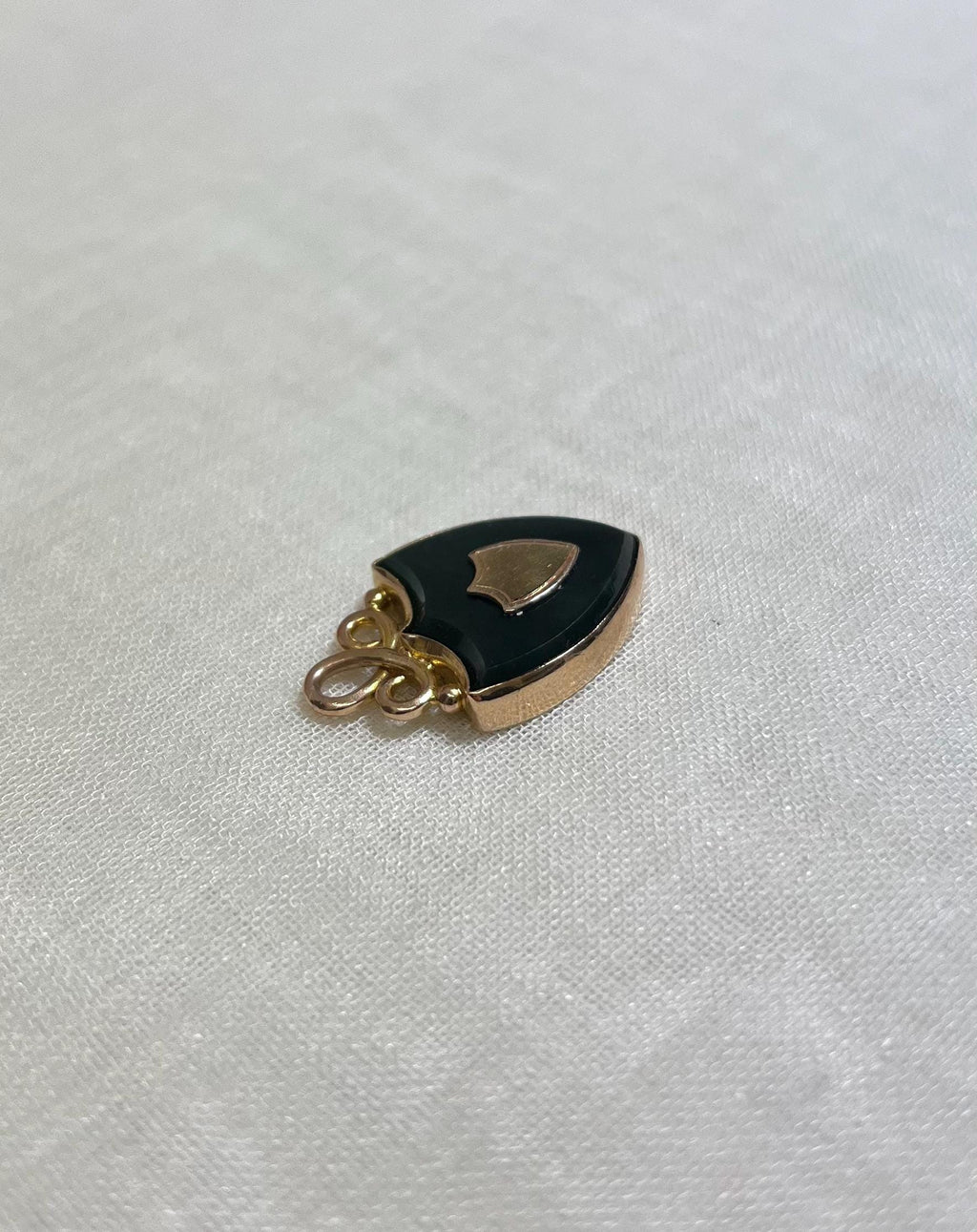 side view of gold shield pendant set with dark bloodstone, on white fabric background 