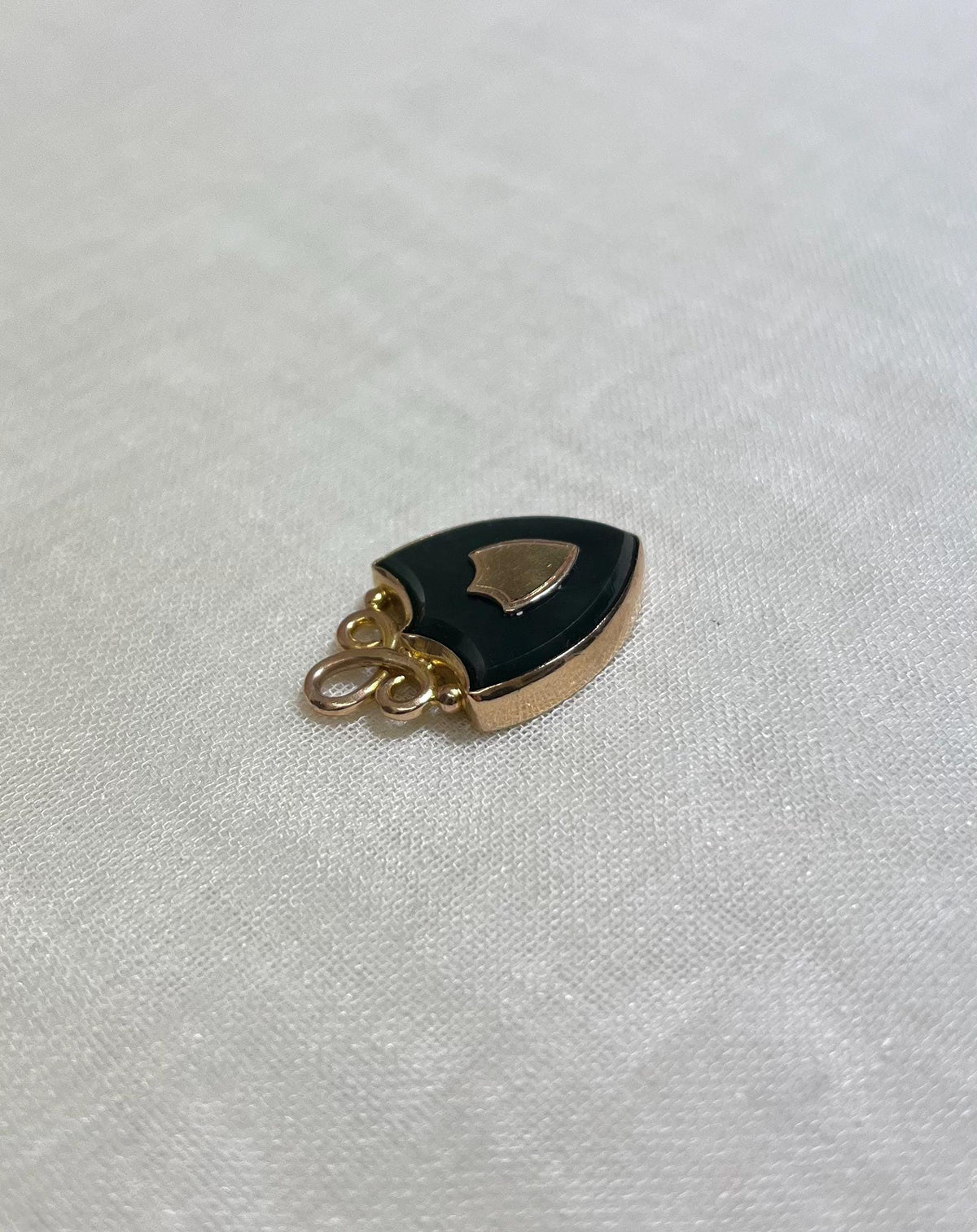 side view of gold shield pendant set with dark bloodstone, on white fabric background 