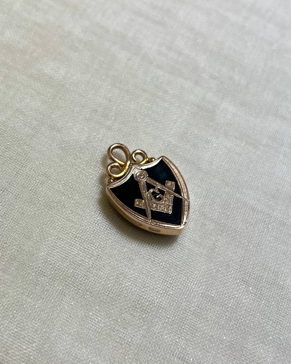gold shield pendant set with dark green bloodstone and gold masonic compass design, on white fabric background