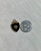 gold shield pendant next to ten pence coin for size reference, on white fabric background