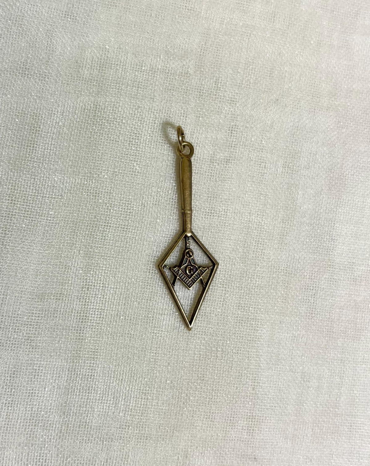 Gold pendant with geometric design on a light fabric background