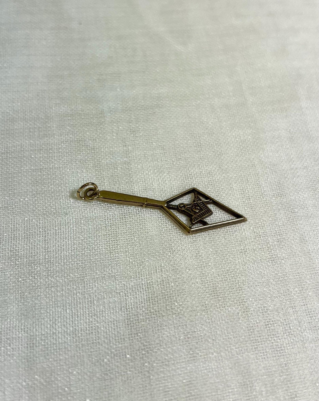 gold charm in the shape of an arrow with masonic symbol inside, resting on white fabric background