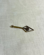 gold charm in the shape of an arrow with masonic symbol inside, resting on white fabric background