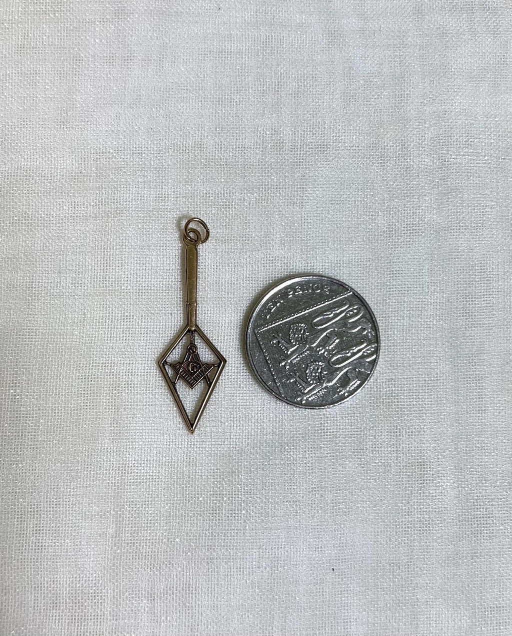 gold pendant next to ten pence coin on white fabric background 
