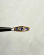gold ring set with blue sapphires and diamonds, held by silver metal tool above soft white background