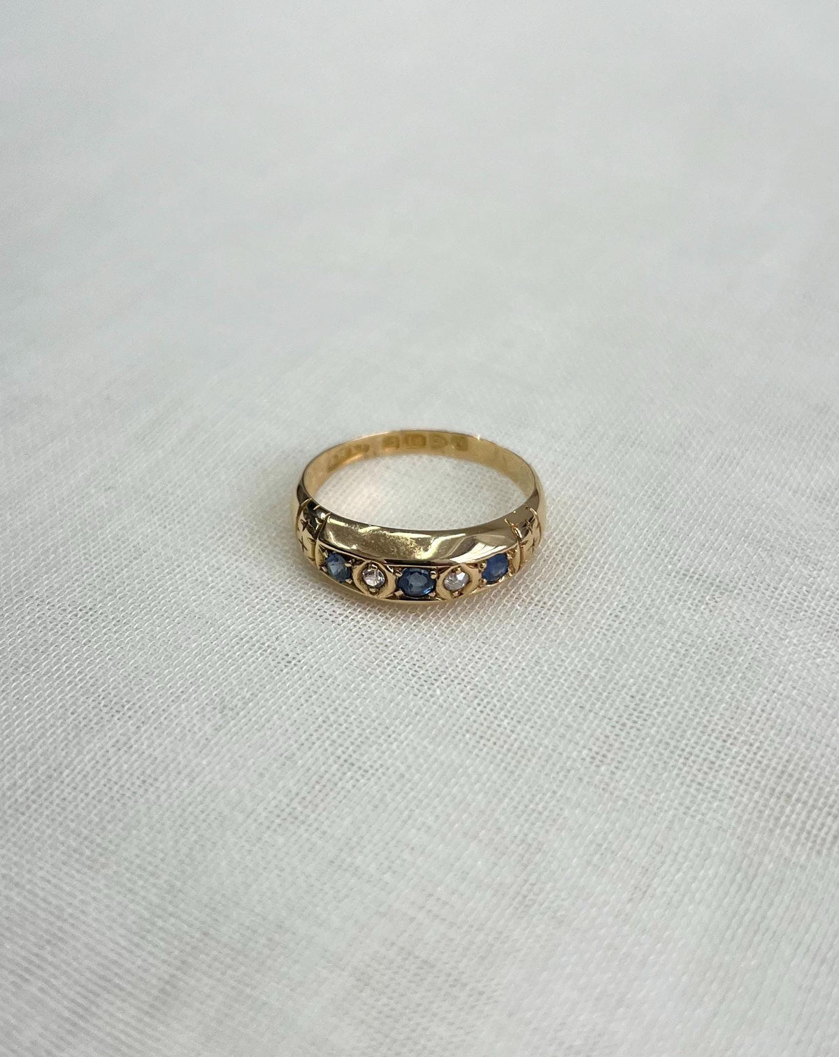 gold band set with blue sapphires and diamonds, resting on white fabric background 