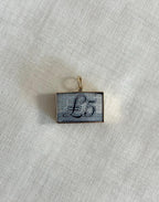 rectangle gold charm with five pound note inside, resting on off white fabric background 