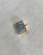 rectangle gold charm with five pound note inside resting on off white fabric background