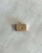 back of rectangle gold charm with hallmark visible, resting on off white  fabric background 