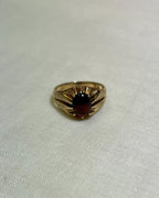 gold ring with dark red garnet stone, on a white fabric background 