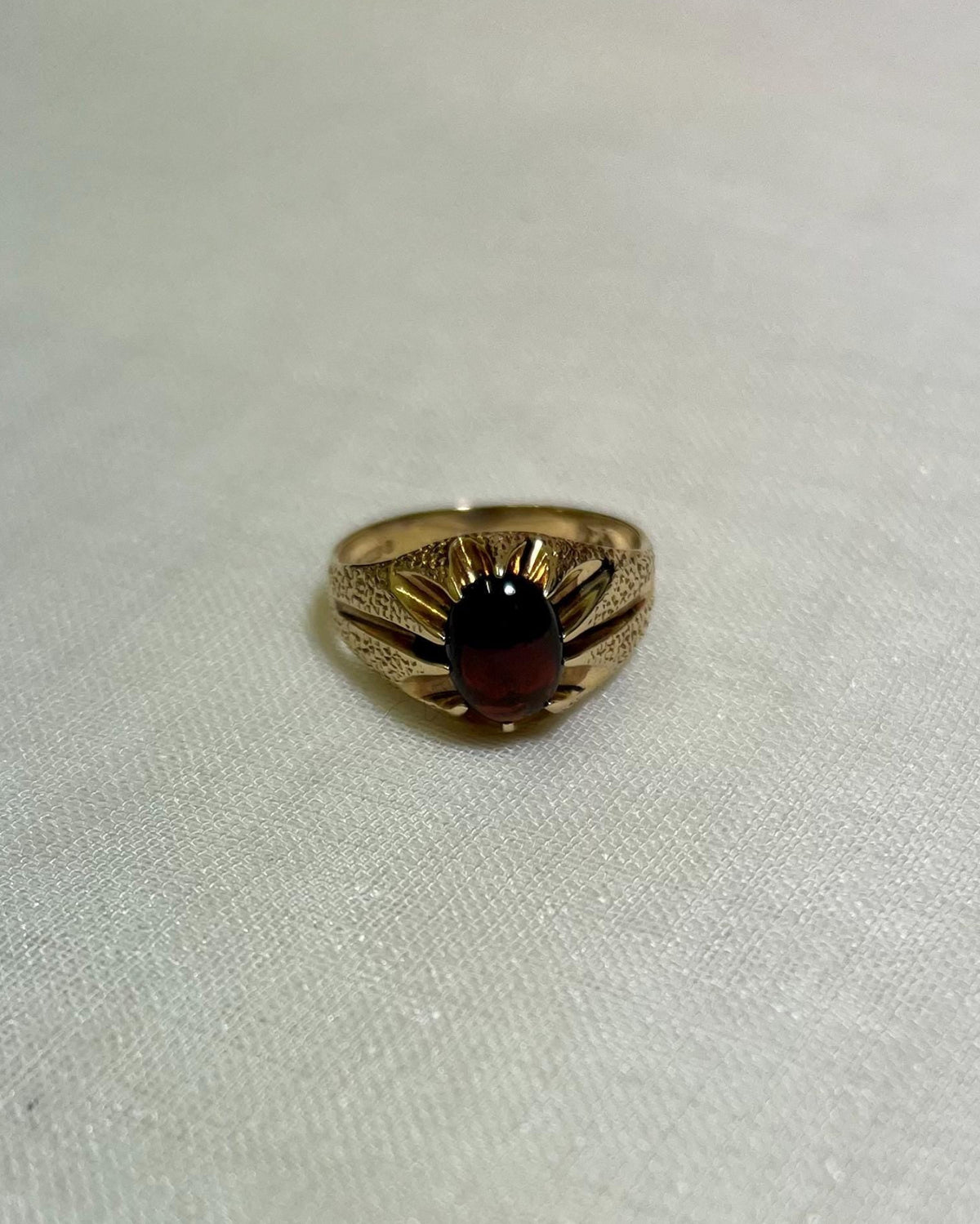 gold ring with dark red garnet stone, on a white fabric background 