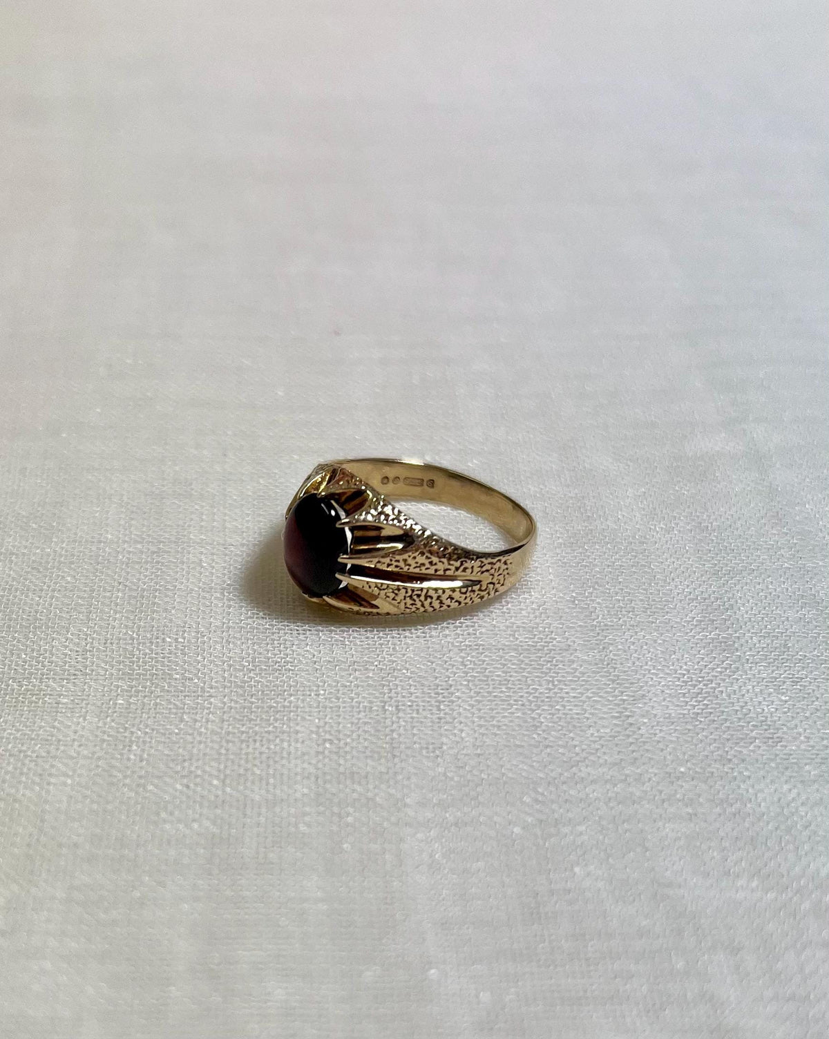 Gold ring with a red gemstone on a white fabric background