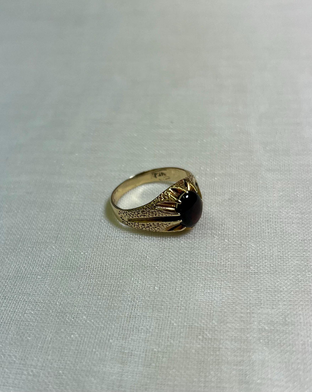 gold ring with dark red gemstone on white fabric background