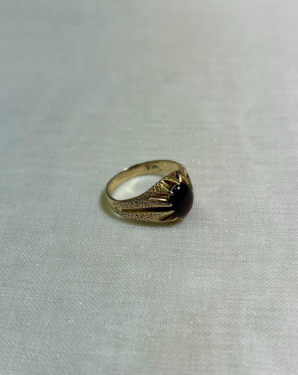 gold ring with dark red gemstone on white fabric background