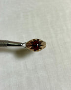 gold ring with textured sides and red stone centre, help by silver tool above cream coloured background 