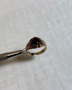 Gold ring with a dark gemstone held by tweezers on a light cream coloured  background
