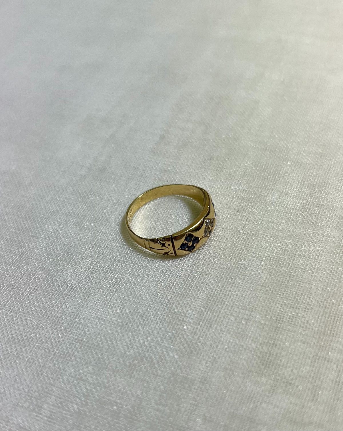 Gold ring with blue embedded gemstones on a white fabric background