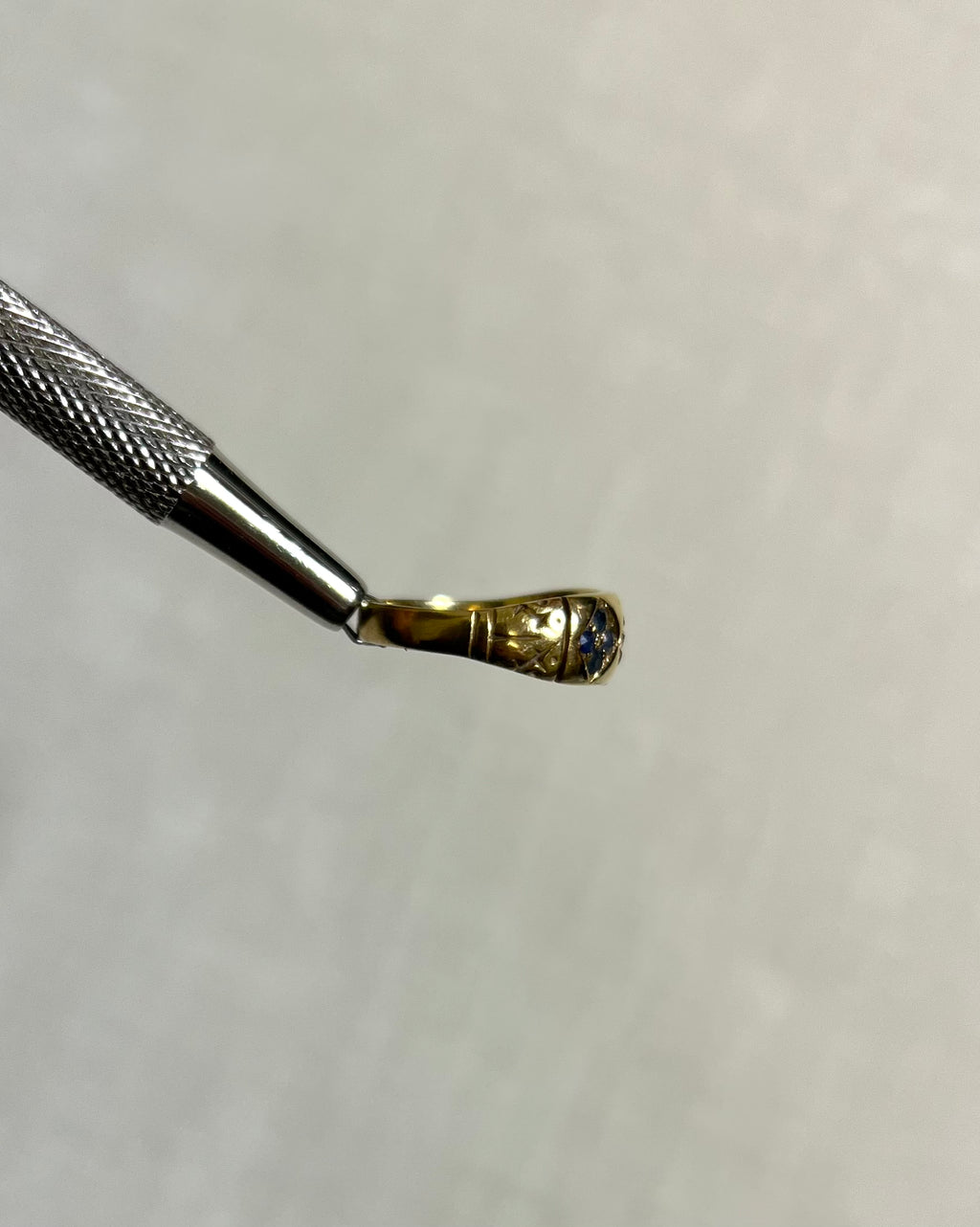side view of gold ring held by silver tool above soft cream background 