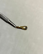 side view of gold ring held by silver tool above soft cream background 