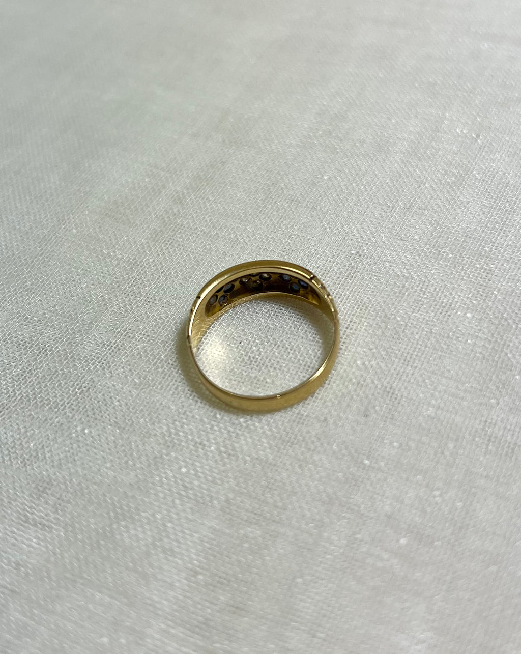 back view of gold ring, resting on white fabric background