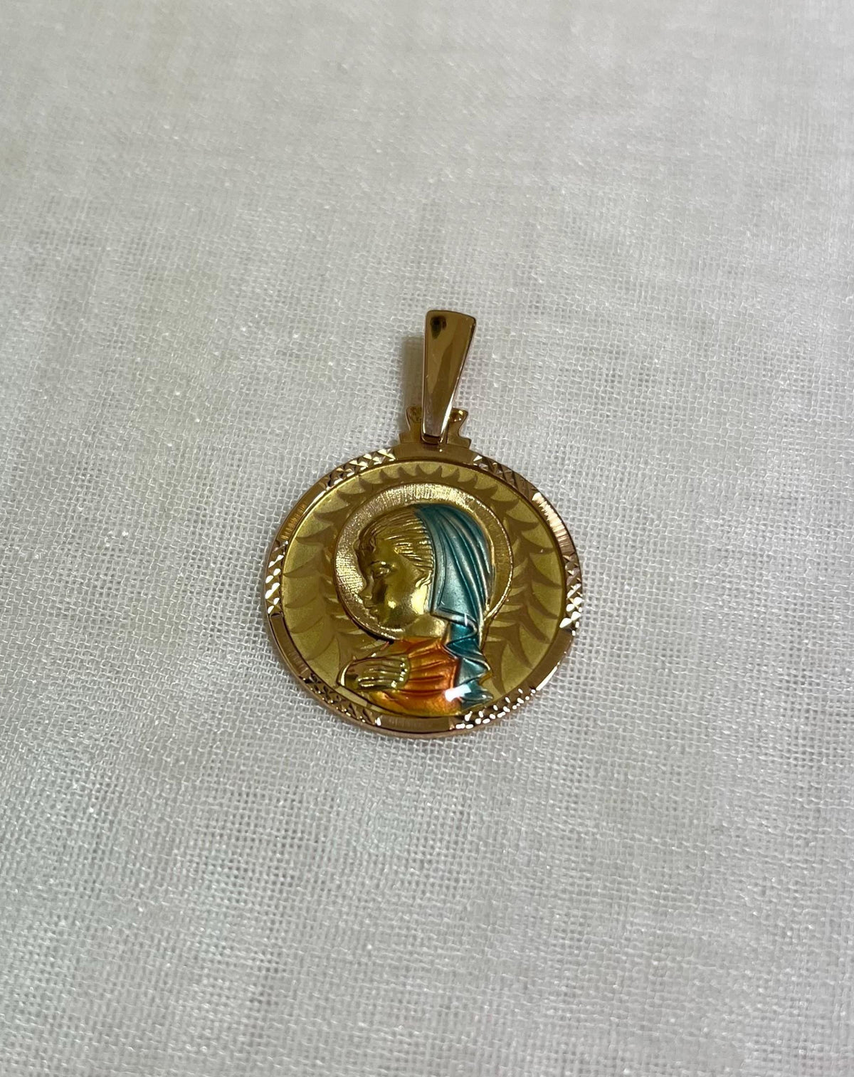 gold disc pendant with enamel Virgin Mary figure, resting on white fabric background