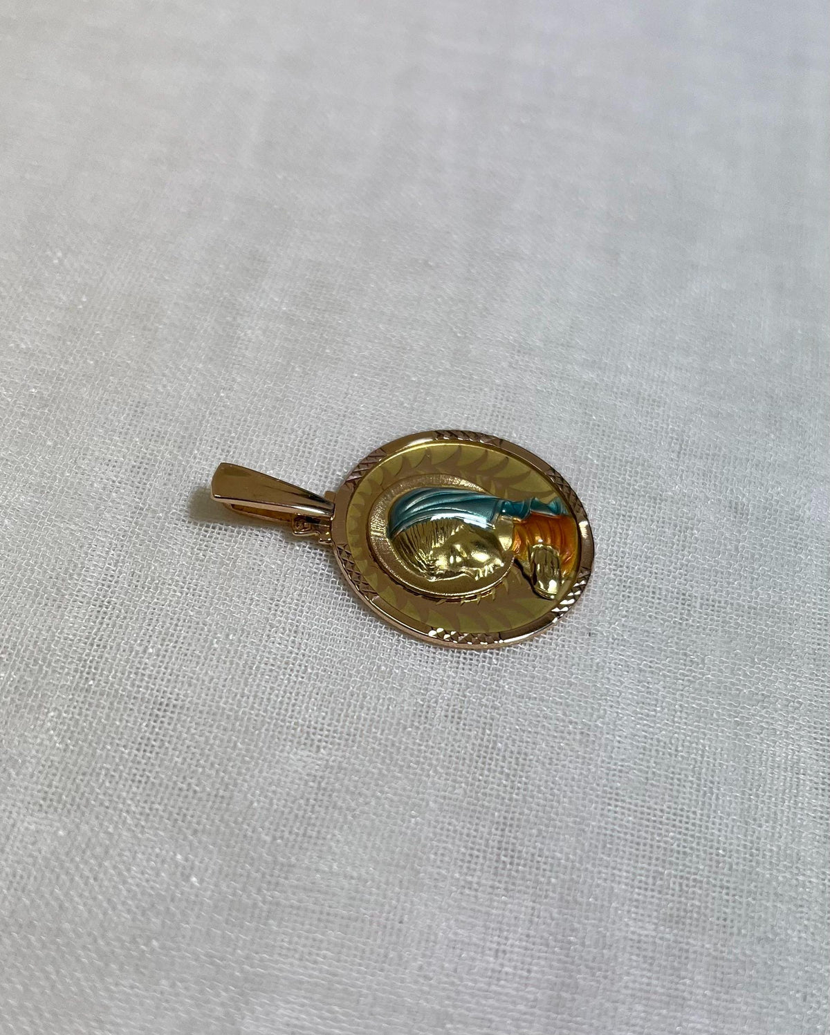 gold disc pendant with enamel Virgin Mary figure, resting white fabric background 