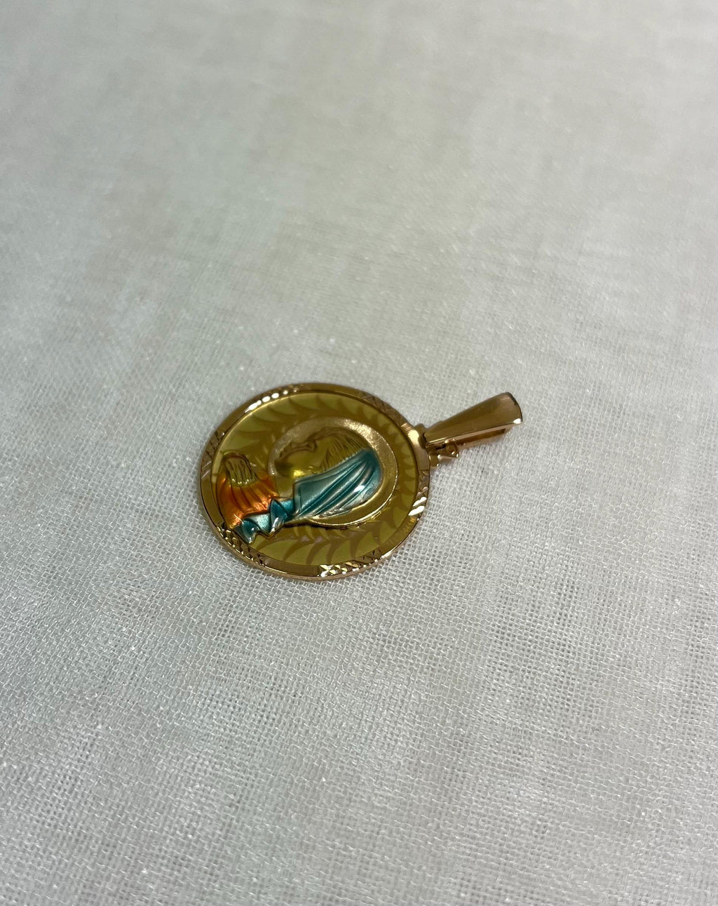 gold disc pendant with enamel Virgin Mary figure, resting on white fabric background 