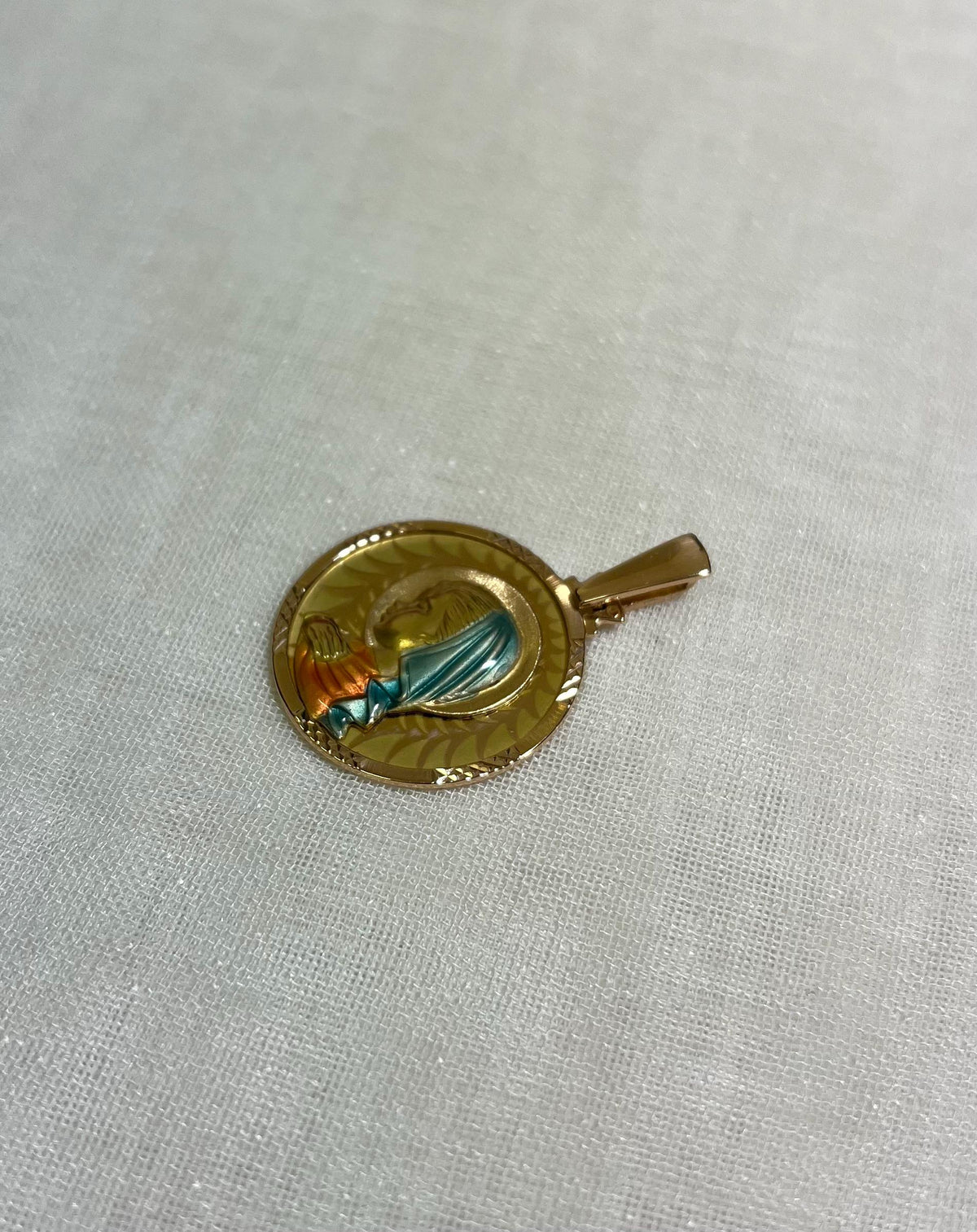 gold disc pendant with enamel Virgin Mary figure, resting on white fabric background 