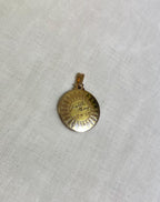 gold disc pendant with name and date engraving, resting on white fabric background 