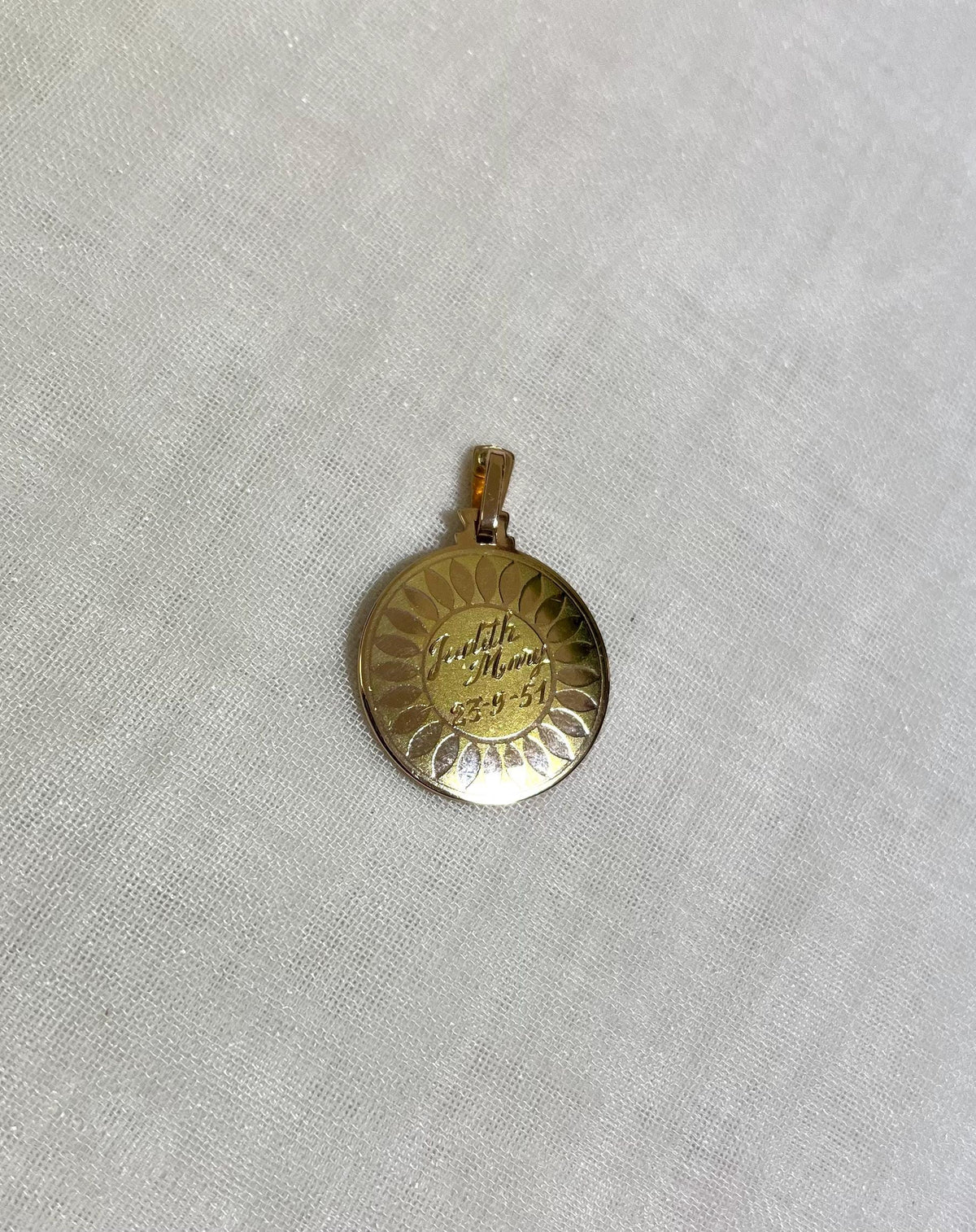 gold disc pendant with name and date engraving, resting on white fabric background 