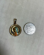 gold pendant with enamel Virgin Mary, next to ten pence coin, on white fabric background