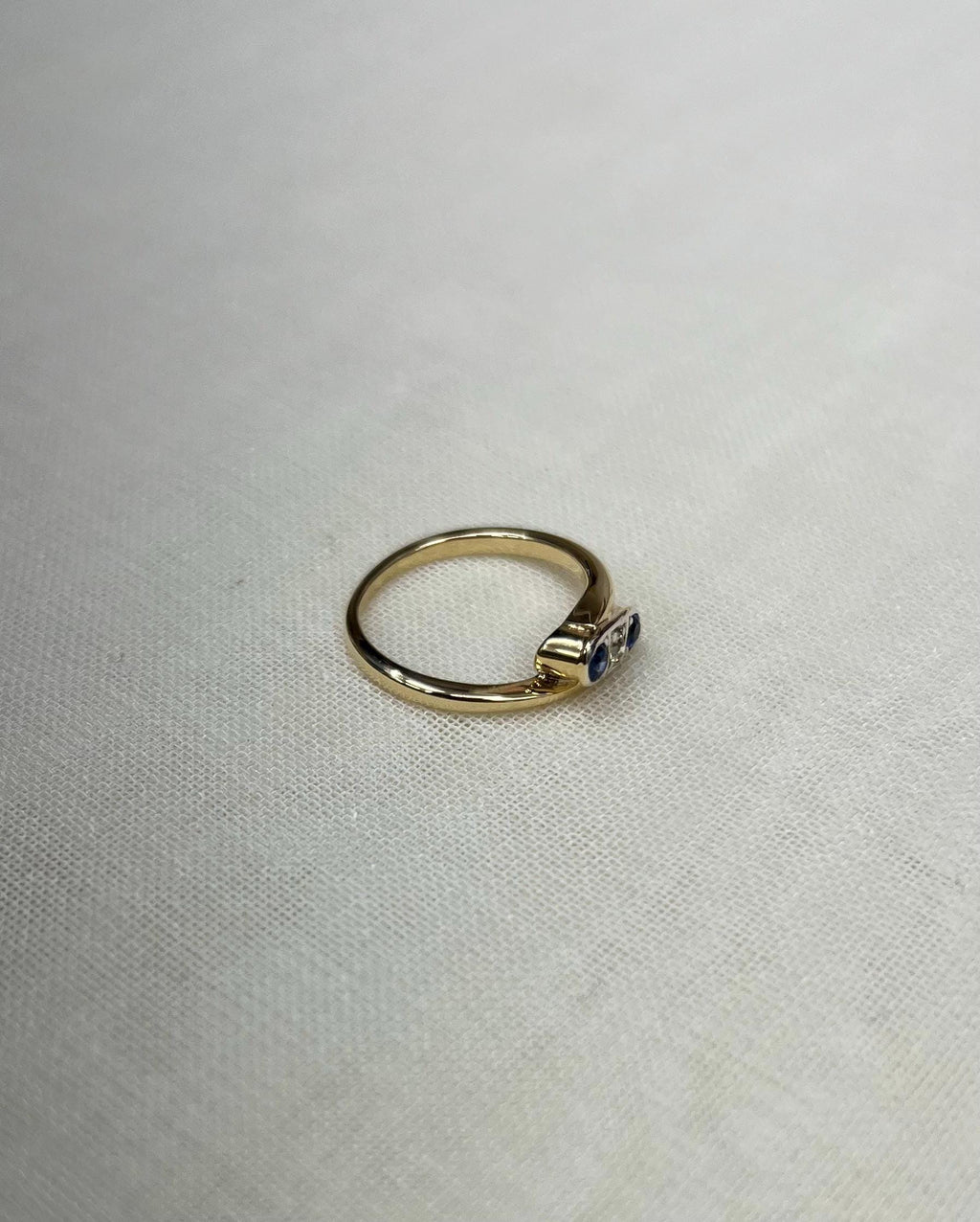 gold ring set with blue and clear stones, resting on white fabric background