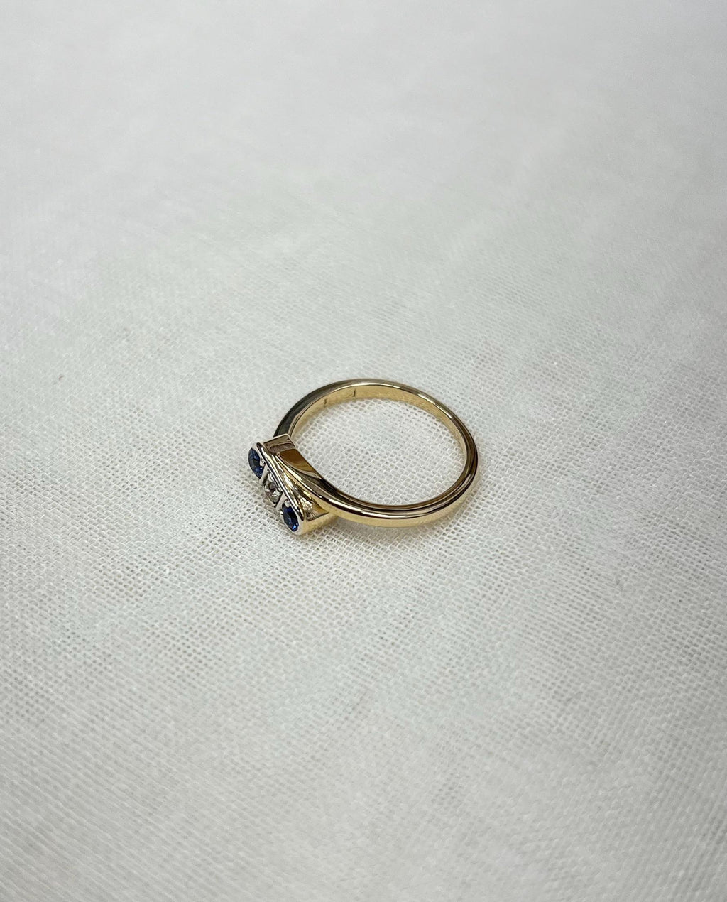 gold trilogy ring with blue sapphires and diamond, resting on white fabric background 