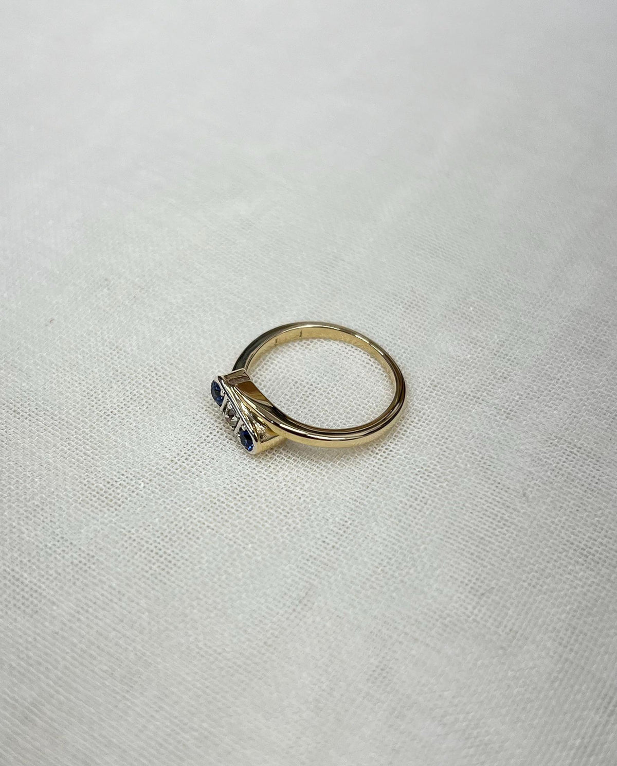 gold trilogy ring with blue sapphires and diamond, resting on white fabric background 