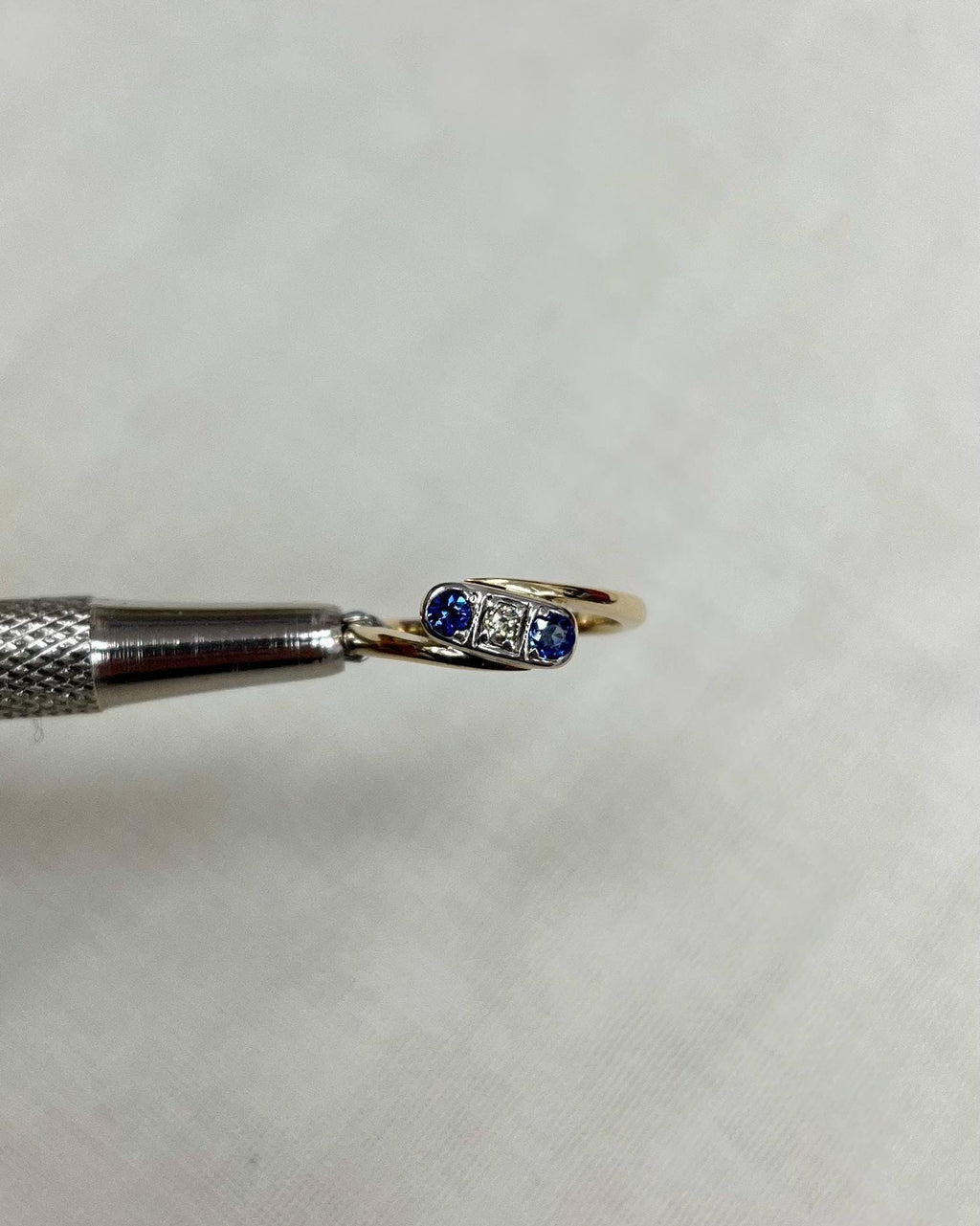 Gold ring with blue gemstones held by tweezers on a white background