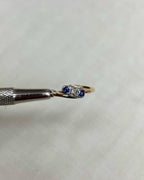 Gold ring with blue gemstones held by tweezers on a white background